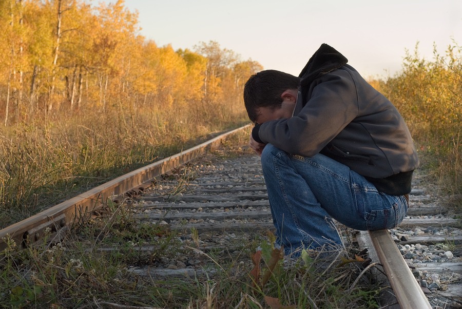 Man With Head Buried in His Lap Sitting on a Railroad Track