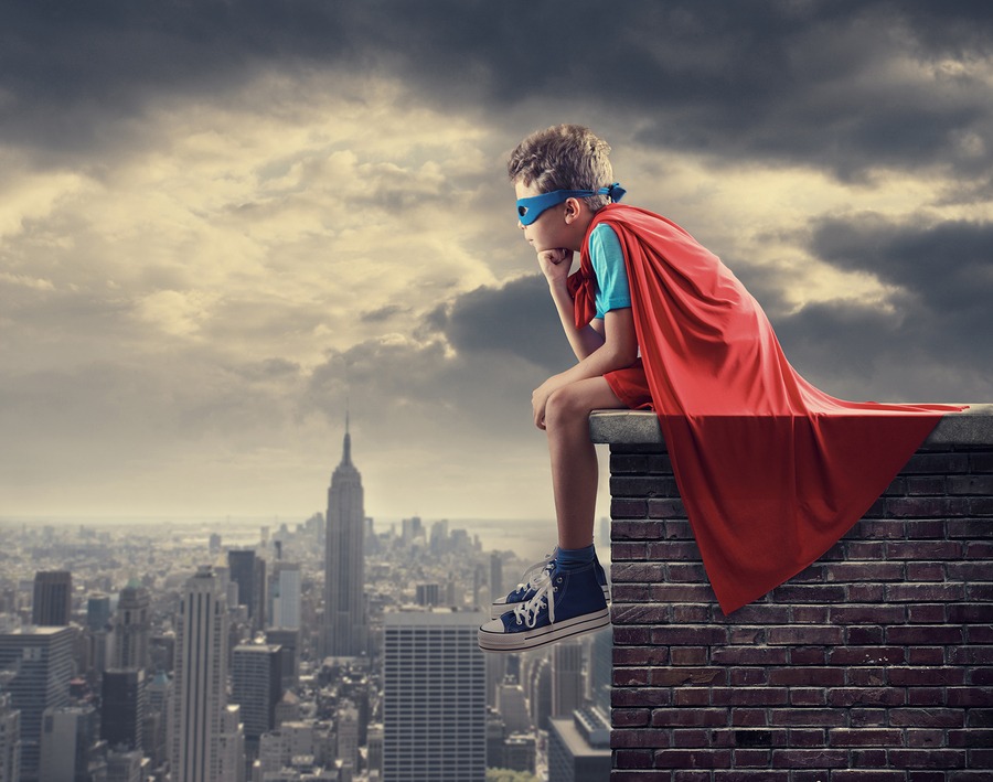 Boy in Superhero Outfit Sitting on a Roof Overlooking A City