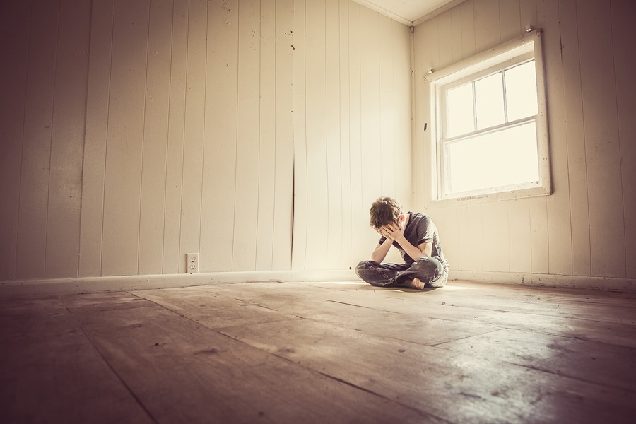 Boy Sitting in Empty Room With Face In HIs Hands