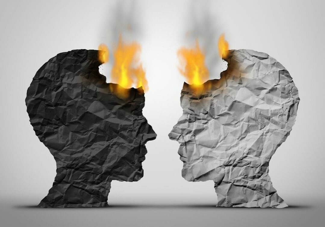 Profiles of Two Faces Made From Paper, One Black and One White, Facing Each Other and Beginning to Catch on Fire