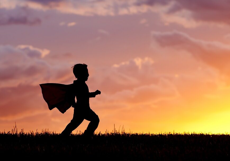 Being your own hero. Silhouette Of A young boy wearing a cape plays a super hero at sunset.