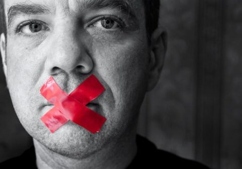 Man in Black and White With Red Tape in an "X" Over His Mouth