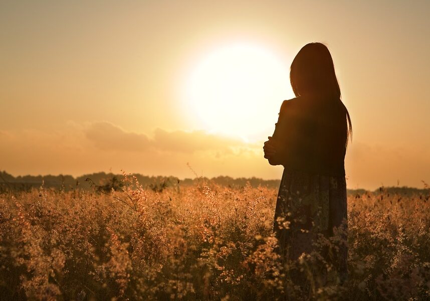 Woman silhouette waiting for summer sun on meadow